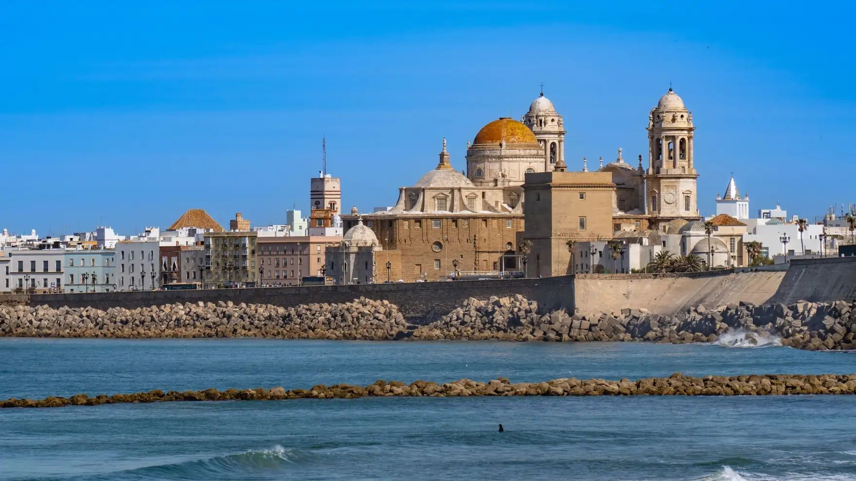 Scenic view of Cádiz Cathedral and waterfront, capturing iconic Andalusian architecture against a clear blue sky