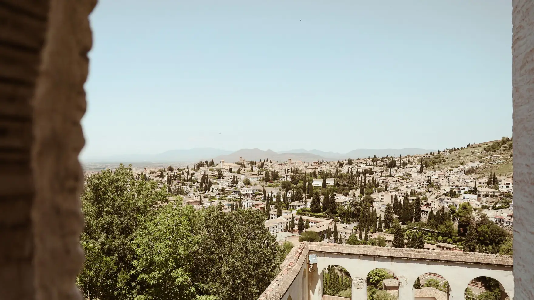 Panoramic view of Granada cityscape framed by historic architecture under a summer sky