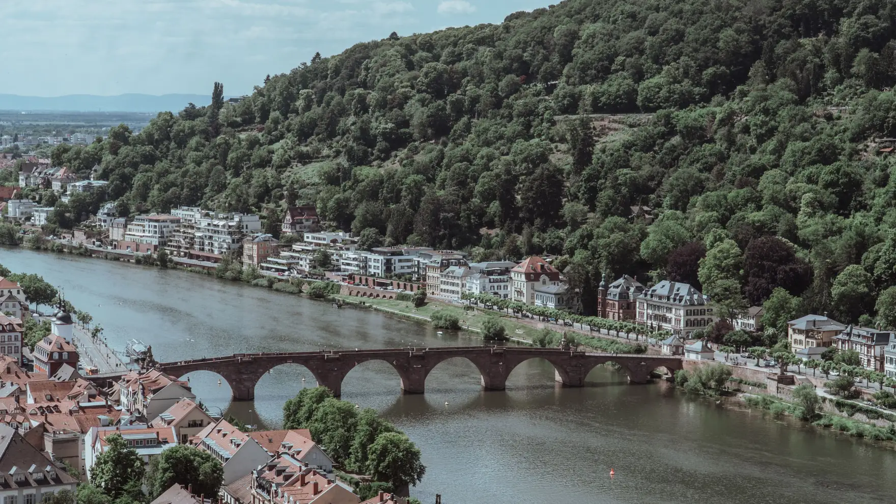 Scenic aerial view of Heidelberg, showcasing its historic bridge over the Neckar River surrounded by lush hills