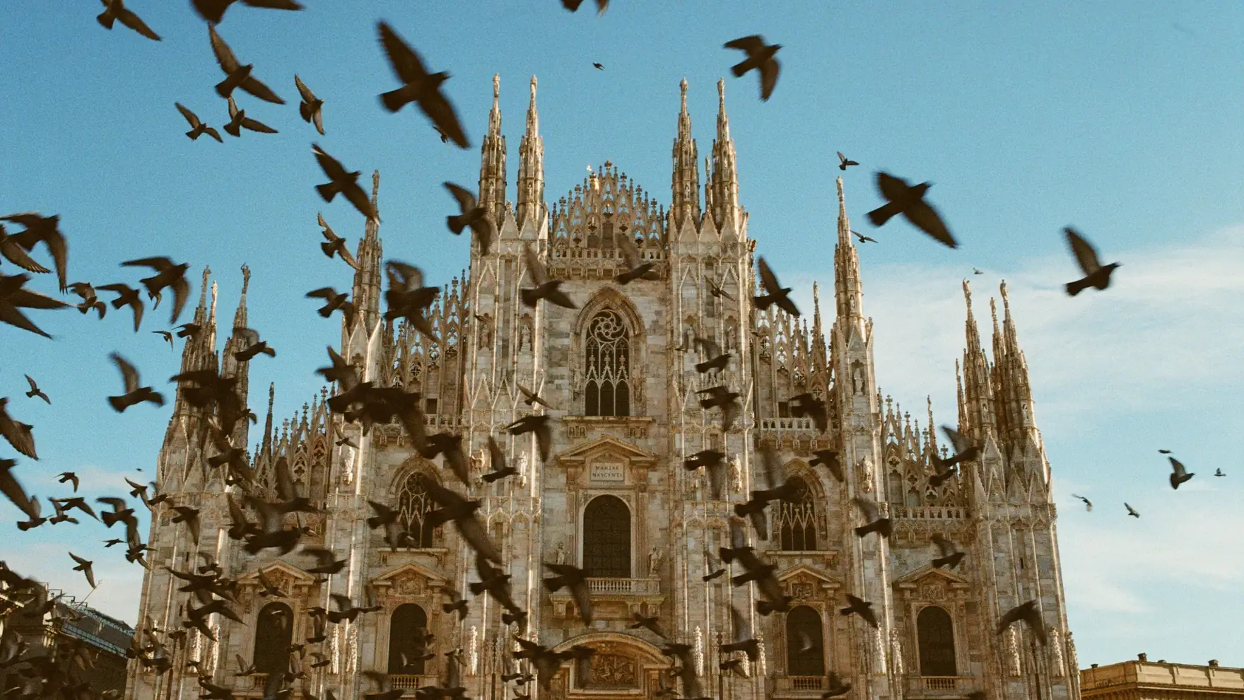 A stunning view of the iconic Milan Cathedral with birds flying against a clear blue sky