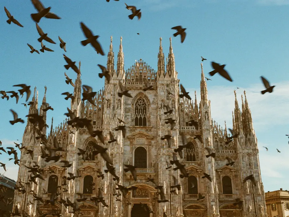 A stunning view of the iconic Milan Cathedral with birds flying against a clear blue sky