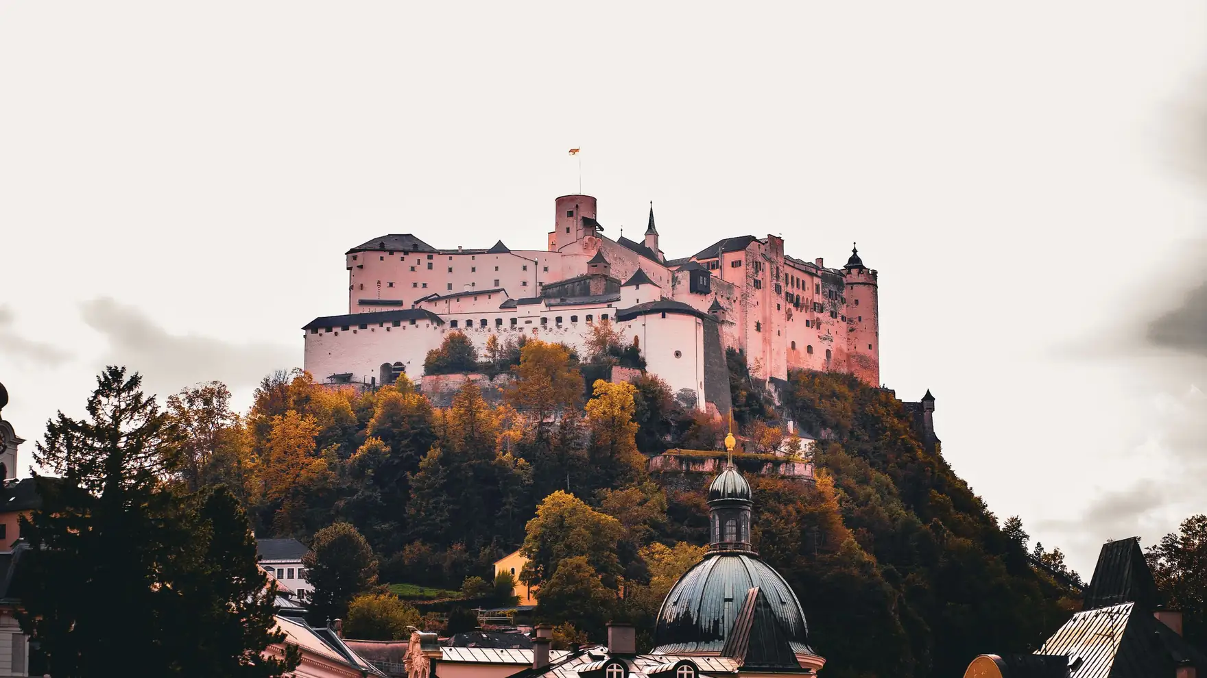 View of the Hohensalzburg Fortress atop a hill surrounded by vibrant autumn foliage in Salzburg, Austria