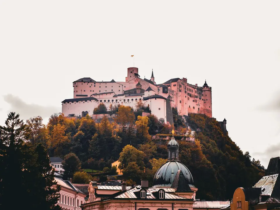View of the Hohensalzburg Fortress atop a hill surrounded by vibrant autumn foliage in Salzburg, Austria
