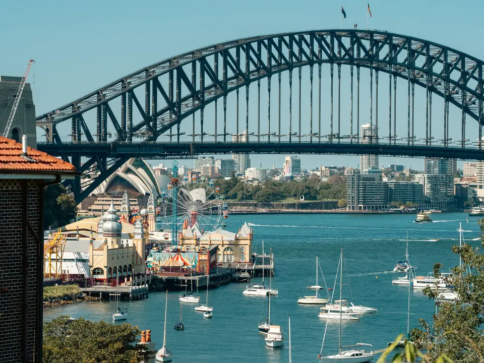 A vibrant view of Sydney Harbour Bridge with Luna Park and sailboats highlighting the iconic skyline